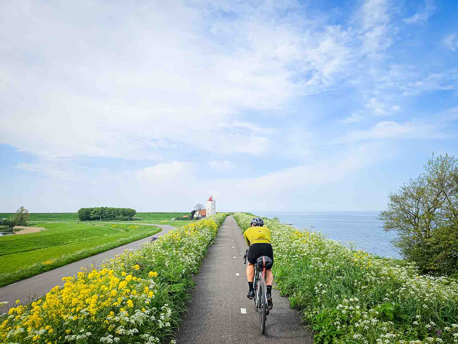 Ein Radfahrer fährt auf einem schönen Radweg neben dem Meer, auf einen Leuchtturm zu