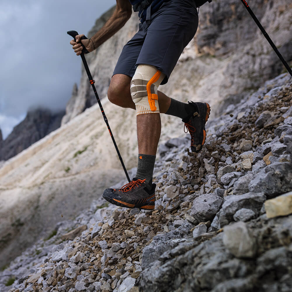 Eine Person trägt eine Wander Kniebandage auf einer Wanderung im Gebirge und läuft einen steilen Berg hinab.