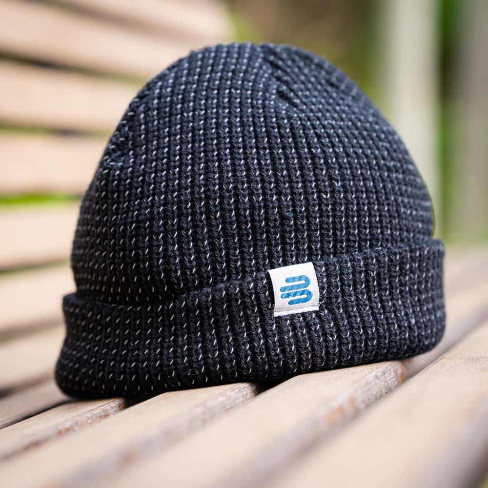 Eine schwarze Bauerfeind Sports Strickmütze mit dem Logo auf einem Holzbank im Freien. Die grobe Strickstruktur sorgt für ein modernes, sportliches Aussehen.